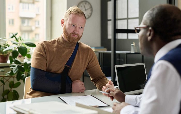 Injured client with an arm sling discussing a personal injury claim with an attorney at an office desk.