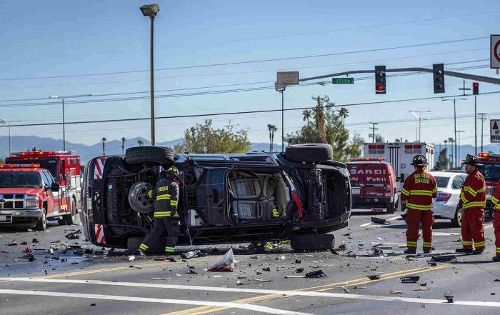 First responders at an intersection car accident scene featuring a rolled-over black SUV and fire trucks.