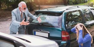An angry driver gesturing at a stressed woman after a car collision, illustrating steps following an uninsured driver accident.